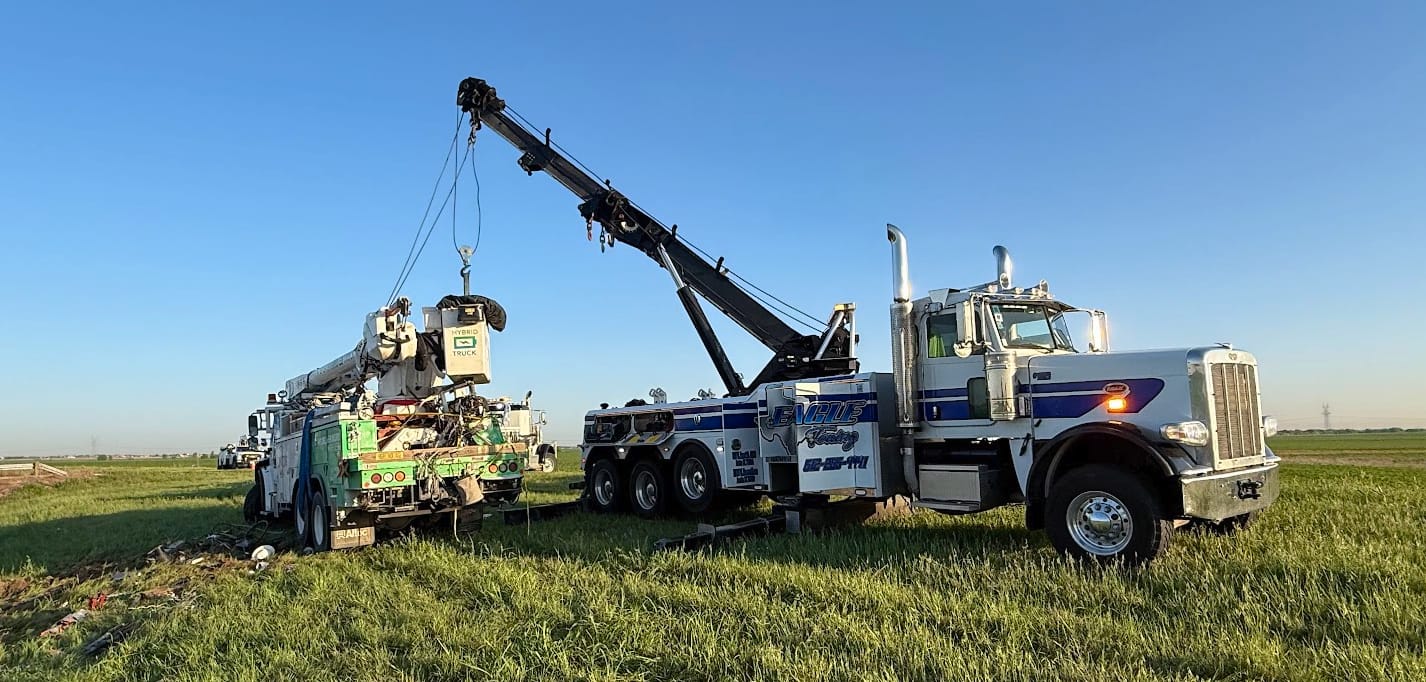 Tow truck rescuing a utility truck in a field.